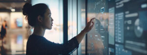 In an office, a woman touches a digital display while evaluating user interface options for Qvidian and Loopio.